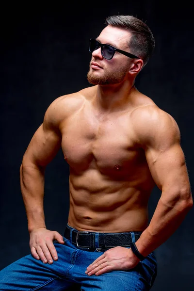 Portrait of a athletic muscular bearded man posing on a black background. Male in glasses showing muscles.