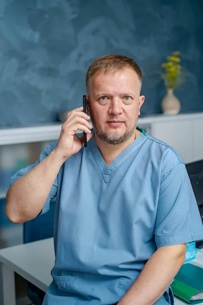 Lekarz Fartuchu Rozmawia Przez Telefon Siedzenie Krześle Gabinecie Lekarskim — Zdjęcie stockowe