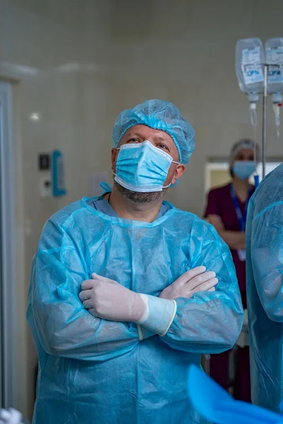 Doctor in scrubs, medical mask and gloves. Surgeon stands cross hands in surgery room.