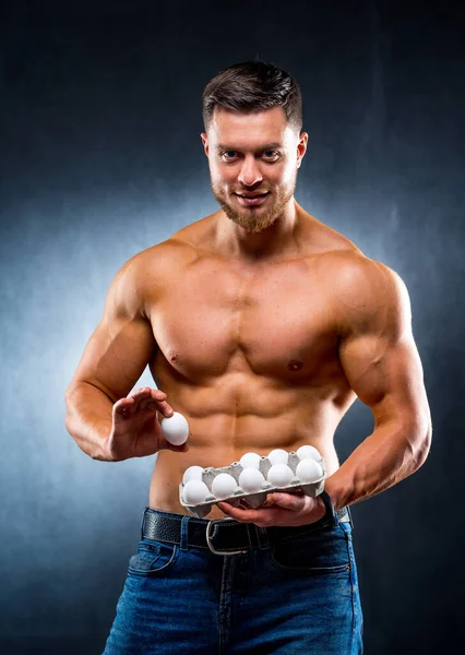 ハンサムな若いスポーツマンは 卵で包装を保持しています 健康食品タンパク質 灰色の背景 卵1個をカメラに見せます 裸の胴 健康的な生活の概念 — ストック写真