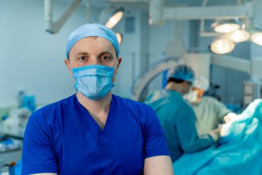 Bir doktor ya da tıp uzmanı portresi. Dikey portre. Önlüklü adam. Ameliyat odasının arka planı aydınlık. Yakın çekim..