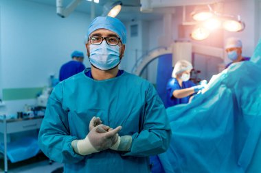 Cerrahi odasında önlüklü bir doktor var. Ellerinde lateks eldivenler. Arka planda robotik ekipman..