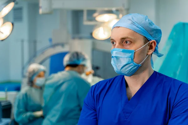 Selective focus on medic in operating room. Mask on face. Blurred background with working team.