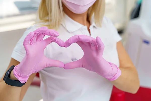 Young blonde surgeon doctor woman over isolated background smiling in love showing heart symbol and shape with hands.