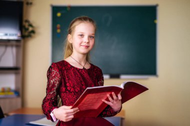 Güzel gülümseyen kız kitap tutuyor. Okula gidiyorum. Portre, sınıf arkaplanı. Öğrenci bir kitaba sarılıyor. Yaşam tarzı, ilgi, hobi, boş zaman, boş zaman.