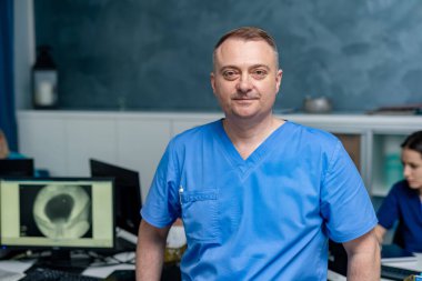 Önlüklü doktor ofisinde duruyor. Sıhhiye kameraya bakıyor. Hastane çalışanı ofisinde..
