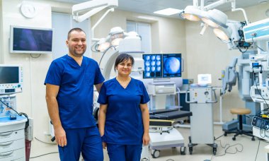 Kadın ve erkek doktor ameliyathanede. Arka planda modern tıbbi ve cerrahi ekipman.