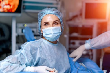 Kadın doktorun koruyucu maske taktığı ve ameliyat odasına karşı poz verdiği baş ve omuz portresi.