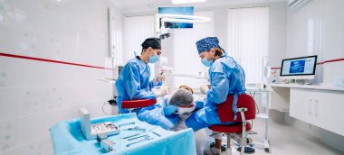 İki dişçi modern stomatoloji kliniğinde hastaların dişlerini muayene ediyor. Yan taraftan seçici odaklanma. Önlüklü dişçiler..