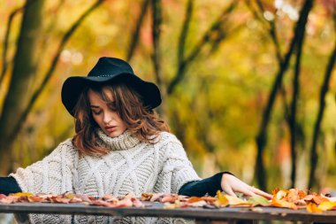Çekici bir gülümsemesi olan siyah şapkalı bir kız. Sonbahar doğasının arka planında parktaki kız..