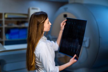 Hastanenin doktoru hastanın röntgen filmini tutuyor. Modern MRI makinesi arka planı. Sağlık, röntgen, insanlar ve tıp konsepti.