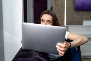 Laptop kullanan çekici bir kızın ön görüntüsü. Önde dizüstü bilgisayar var. Güzel gözlü bir kadın. Evden çalış..