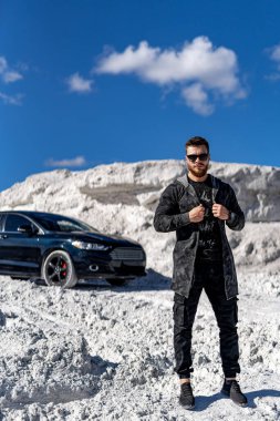 Beyaz kayaların arkasında, arabanın yanında yakışıklı bir adam var. Şık fotosoplama.