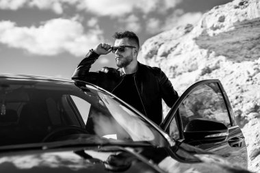 Yolda duran yakışıklı adam, arabasının kapısını açtı. Siyah beyaz fotoğraf.