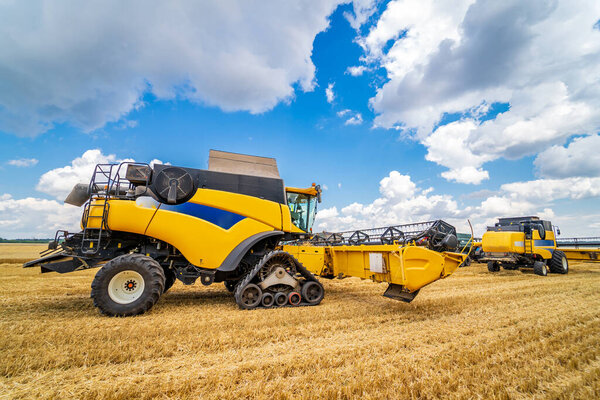 Сельскохозяйственная техника собирает урожай на полях. Специальная техника в действии. Сельскохозяйственная техника в поле. Тяжелая техника, голубое небо над полем.