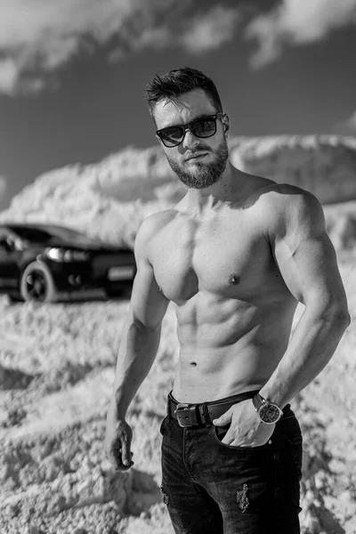 非常に筋肉スポーティな男のカメラを見て 採石場で完璧な体を持つ恥知らずな男 白黒写真 背景に黒い車 — ストック写真