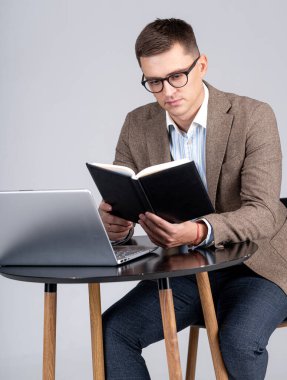Erkek satış müdürü not defterinde çizelgesini kontrol ediyor. Laptop masanın üstünde. İş yerinde profesyonel..