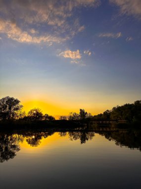 Arka planda ağaçlar olan bir gölün üzerinde güzel bir gün batımı.