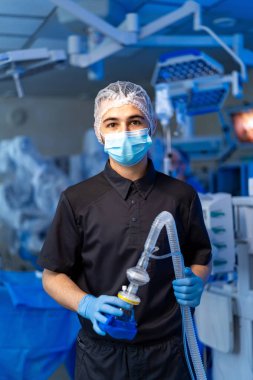 Doktor prosedüre hazırlanıyor. Bir tıbbi uzman ameliyat odasında anestezi cihazıyla ayakta duruyor. Ameliyat sırasında hasta bakımına hazır..