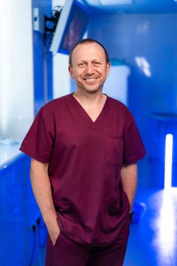 Önlüklü doktor parlak klinikte gülümsüyor. Bordo önlüklü bir sağlık çalışanı, parlak bir klinikte, sıcak bir şekilde gülümsüyor..