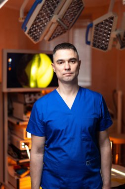 Mavi önlüklü cerrah, ameliyathane. Odaklanmış bir cerrah iyi donanımlı bir ameliyathanede ameliyata hazır bekliyor..