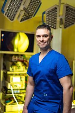 Cerrah ameliyathanede dimdik ayakta duruyor. Mavi önlüklü bir cerrah, gelişmiş tıbbi ekipmanlarla çevrili bir ameliyathanede duruyor..