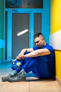 Renkli koridorda hemşire. Mavi önlüklü bir hemşire canlı bir duvara yaslanmış, hastane koridorunda dinleniyor..