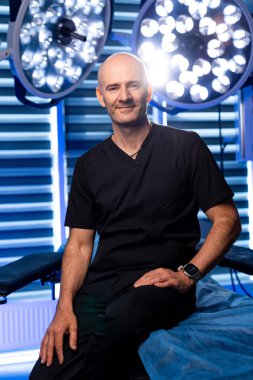 Cerrah, parlak cerrahi odasında poz veriyor. Rahat bir cerrah modern bir ameliyathanede oturur. Etrafı ışık ve tıbbi malzemelerle çevrilidir..