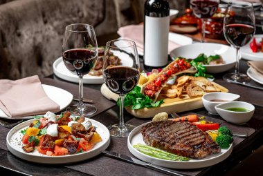 Kırmızı şarapla nefis bir gurme yemeği. Çeşitli gurme yemekleri ve kırmızı şarap kadehleriyle dolu bir masa seti, harika bir yemek deneyimi sunuyor..