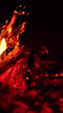 Kamp ateşi söndü ve çok az ateş yanıyor. Közler sopayla hareket eder ve güzel kıvılcımlar yükselir. Kapatın. Siyah zemin. Dikey video