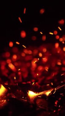 Ateşli közlere dokunuyorum. Parlak kıvılcımlar uçuşur ve küçük alevler ortaya çıkar. Kapatın. Dikey video