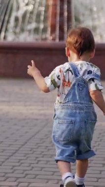 Çocuk dışarıda parkta koşuyor. Küçük çocuk dışarıda koşuyor. Dikey video