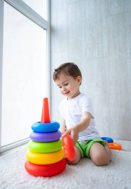 Çocuk oyuncakları istiflemekle oynuyor. Genç bir çocuk parlak bir odanın penceresinin yanında otururken rengarenk yüzükler takmaktan zevk alır..