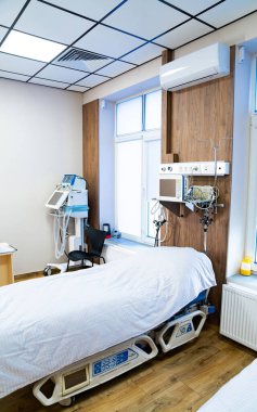 Modern hastane odası düzeneği. Temiz ve düzenli bir hastane odası. İçinde yatak, tıbbi aletler ve pencereden gelen doğal ışık var..