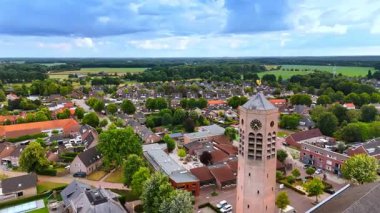 Yazın sakin bir köyün genel görünümü. Resimli bir köy yemyeşil, antika evler ve bulutlu bir gökyüzünün altında göze çarpan bir saat kulesine sahiptir..