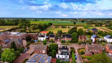 Kırsal kesimde tarlalar ve evler. Parlak mavi gökyüzünün altındaki evleri çevreleyen yemyeşil alanlar kırsal yaşamı gözler önüne seriyor..