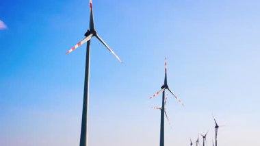 Türbinler enerjiyi dizginler. Rüzgâr türbinleri, açık bir arazide yenilenebilir enerjiyi kullanan açık mavi bir gökyüzünün altında dimdik duruyorlar..