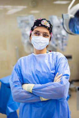 Tıbbi personelden cerrahi hazırlık. Önlük ve maske giyen bir tıp uzmanı ameliyata hazır bir ameliyathanede güvenle duruyor..
