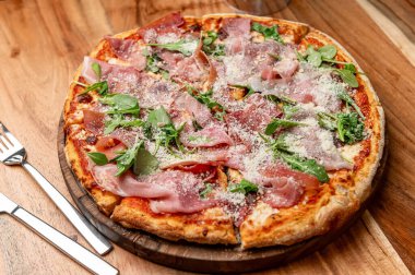 Lezzetli ahşap kaplı pizza! Tahta bir tahtanın üzerinde prosciutto, roka ve parmesan peyniri ile kaplı ahşap kaplı bir pizza servis edilir..
