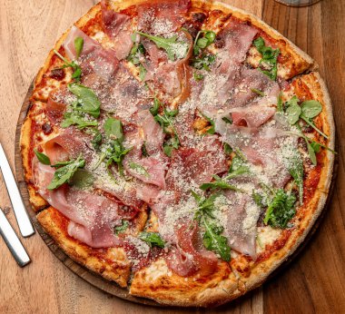 Prosciutto ve roka pizzası. Taze yapılmış pizza özellikleri prosciutto, roka ve ahşap masaya serpiştirilmiş peynir, nefis bir yemeği davet ediyor..