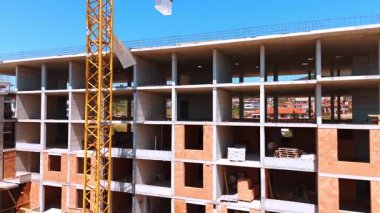 Çok katlı bina devam ediyor. İşçiler açık mavi gökyüzünün altında bir vinç bulunan çok katlı bir bina inşa ediyorlar..