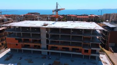 Denize bakan inşaat alanı. İşçiler, etrafları bina ve vinçlerle çevrili bir deniz kenarı şantiyesinde meşguller..