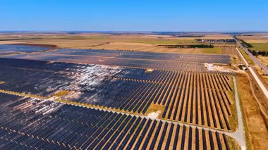 Alanlarda geniş güneş panelleri. Kırsal bir alandaki güneş panelleri güneş ışığını yakalıyor, temiz bir gökyüzü altında yenilenebilir enerji üretimini vurguluyor.