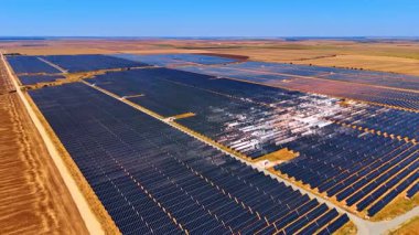 Açık arazide geniş bir güneş çiftliği. Güneş panelleri açık mavi gökyüzünün altında geniş bir alan boyunca uzanıyor, kırsal alanda yenilenebilir enerji sergiliyor..