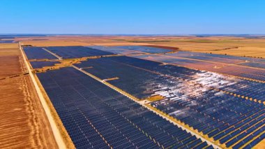 Açık mavi gökyüzündeki güneş enerjisi alanı. Parlak mavi gökyüzünün altında geniş bir güneş paneli uzanır ve enerji üretimi için güneş ışığını yakalar..