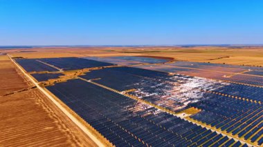 Güneşli arazide geniş bir güneş çiftliği. Güneş panelleri, parlak mavi bir gökyüzünün altında verimli bir şekilde yenilenebilir enerji üreterek araziye yayılıyor..