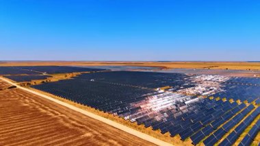 Açık gökyüzü altında geniş bir güneş çiftliği. Geniş güneş panelleri, parlak mavi bir gökyüzünün altında, yenilenebilir enerji üretimini sergiliyor..