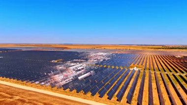 Tarlalar boyunca güneş panelleri. Güneş panelleri açık mavi gökyüzünün altında parlayan tarım arazisini kaplar..