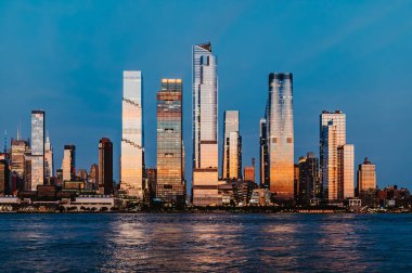 Manhattan gökyüzü alacakaranlıkta parlıyor. Manhattan rıhtımında uzun binalar var. Akşam güneşi batarken cam yüzeylerden yansıyor..