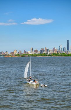 Yelkenli New York şehrinin silueti boyunca ilerliyor. Bir yelkenli, açık bir günde arka planda Manhattan silueti olan suda süzülüyor..